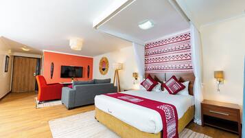 A modern hotel room with a large bed, a sofa, a TV, and a wooden floor.