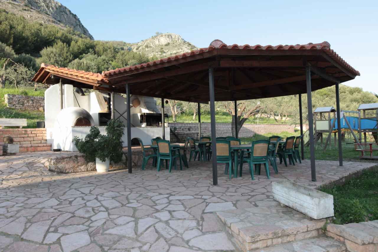 Um pátio externo com piso de pedra, cadeiras verdes e um forno de tijolos.