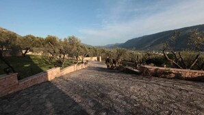 A stone pathway leading through a landscaped area with trees and a view of distant hills. - Almini Apartments (Igoumenitsa)