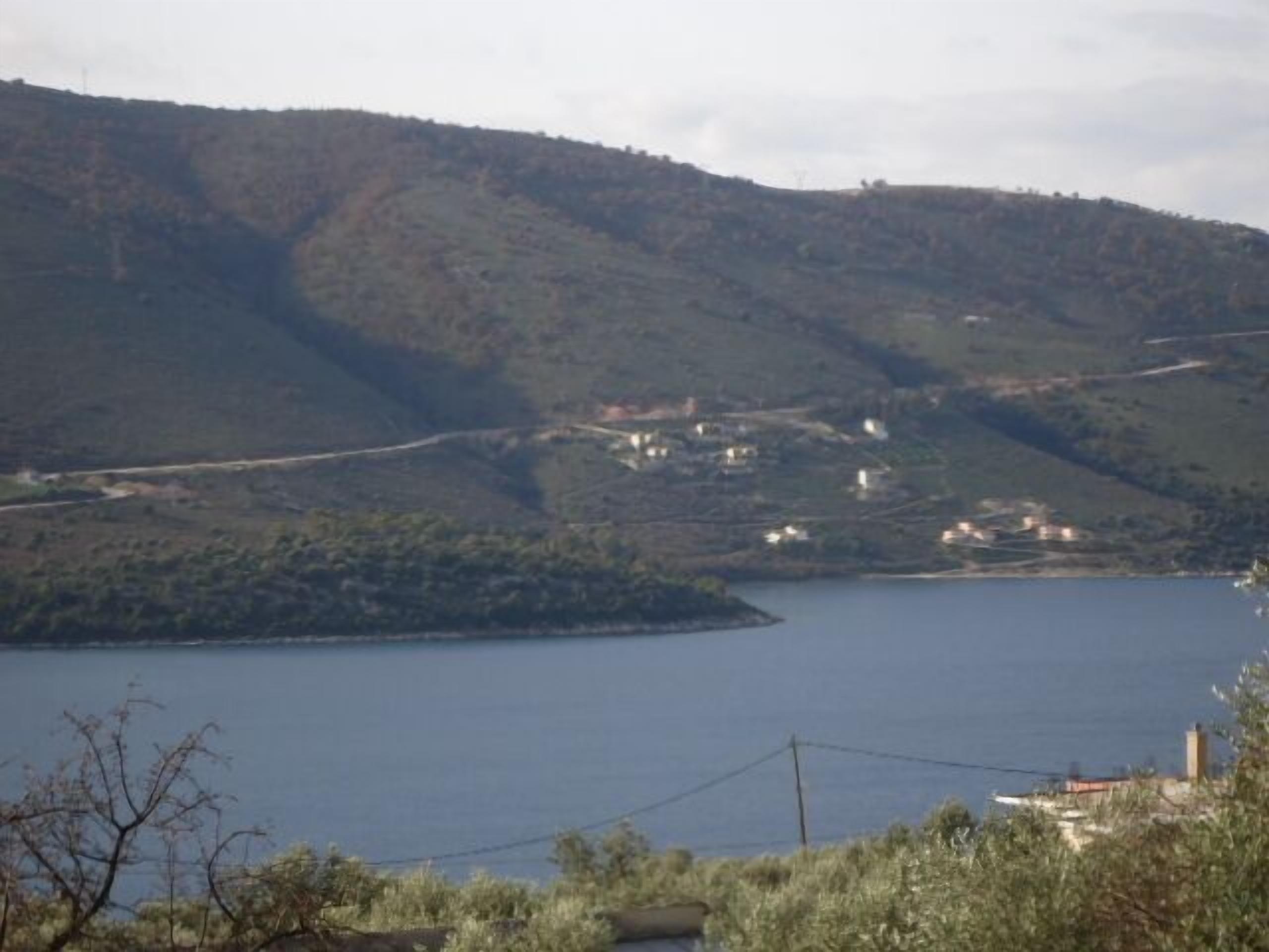Un paisaje costero con una masa de agua, colinas y edificios dispersos.