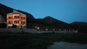 A multi-story building with balconies, surrounded by a landscaped area and hills. - Almini Apartments (Igoumenitsa)