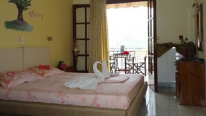 A hotel room with a bed, a window with curtains, a balcony with a table and chairs, and a wall with a tree illustration. - Almini Apartments (Igoumenitsa)