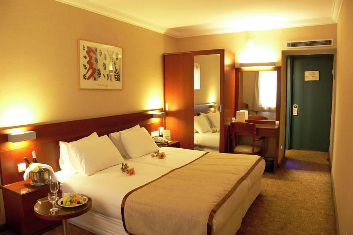 A hotel room with a large bed, bedside tables, a desk, a chair, a mirror, and a door.