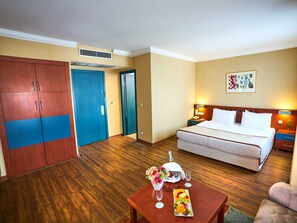 A hotel room with a bed, a nightstand, a table with a fruit platter and flowers, a wooden wardrobe, and a door. - Feronya Hotel (Istanbul)