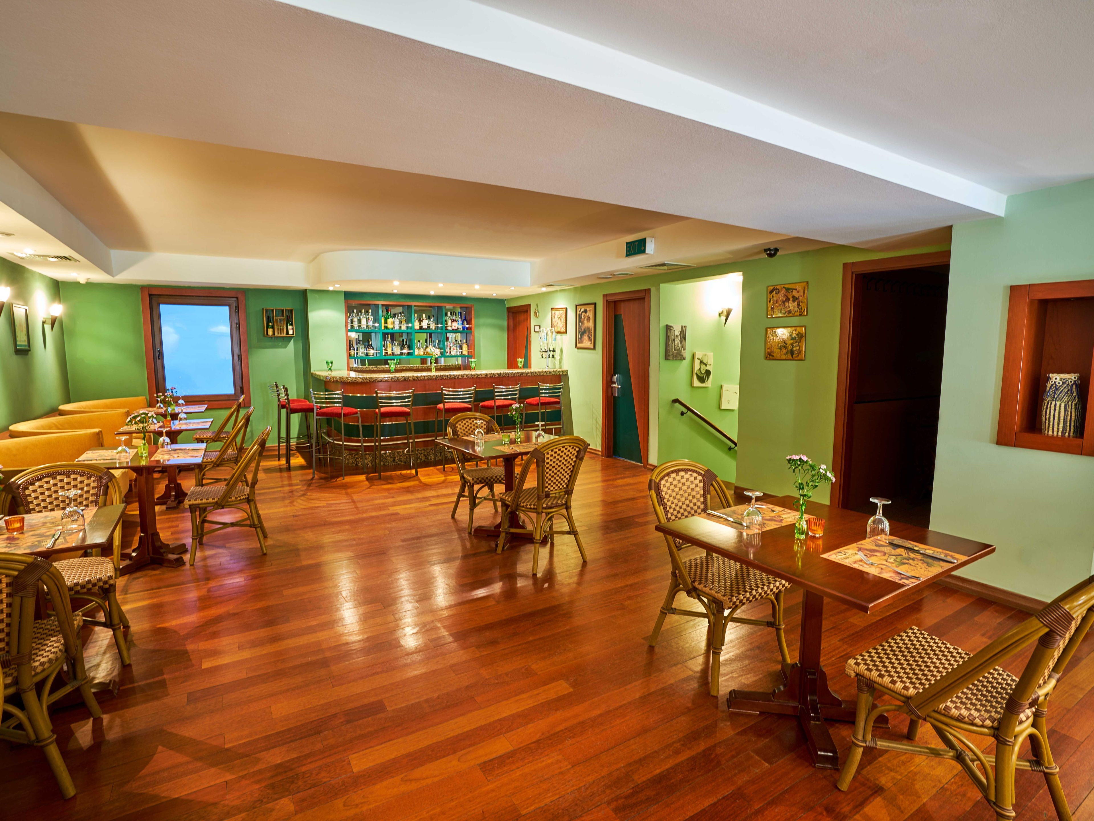 Un restaurant doté d’un plancher en bois, de chaises en osier, d’un bar et de murs peints en vert.