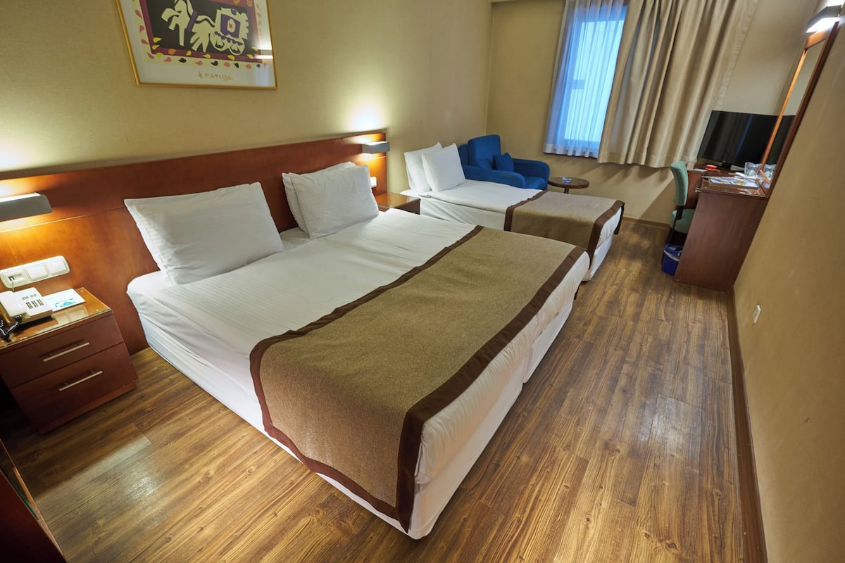 A hotel room with two beds, a desk, a chair, a television, and a window with curtains.