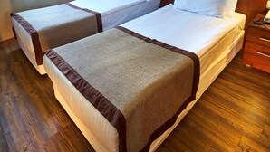 A hotel room with two beds, a wooden floor, a painting on the wall, and a window with curtains. - Feronya Hotel (Istanbul)