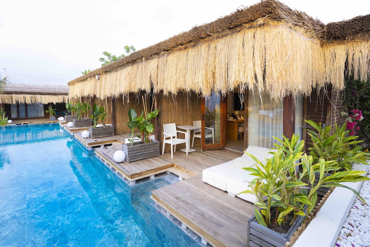 Un área junto a la piscina con terraza de madera, sillones de descanso y una estructura de techo de paja.