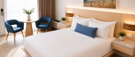 A hotel room with a large bed, two chairs, a small table, and a painting on the wall.