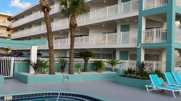 Un hotel con piscina, palmeras y un edificio de varios pisos con balcones.