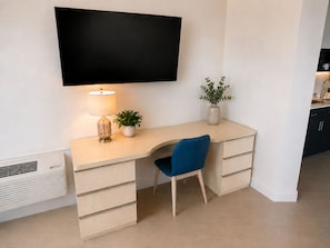 Habitación moderna y minimalista con una televisión de pantalla plana en la pared, un escritorio con una lámpara, una silla y una pequeña planta en maceta.