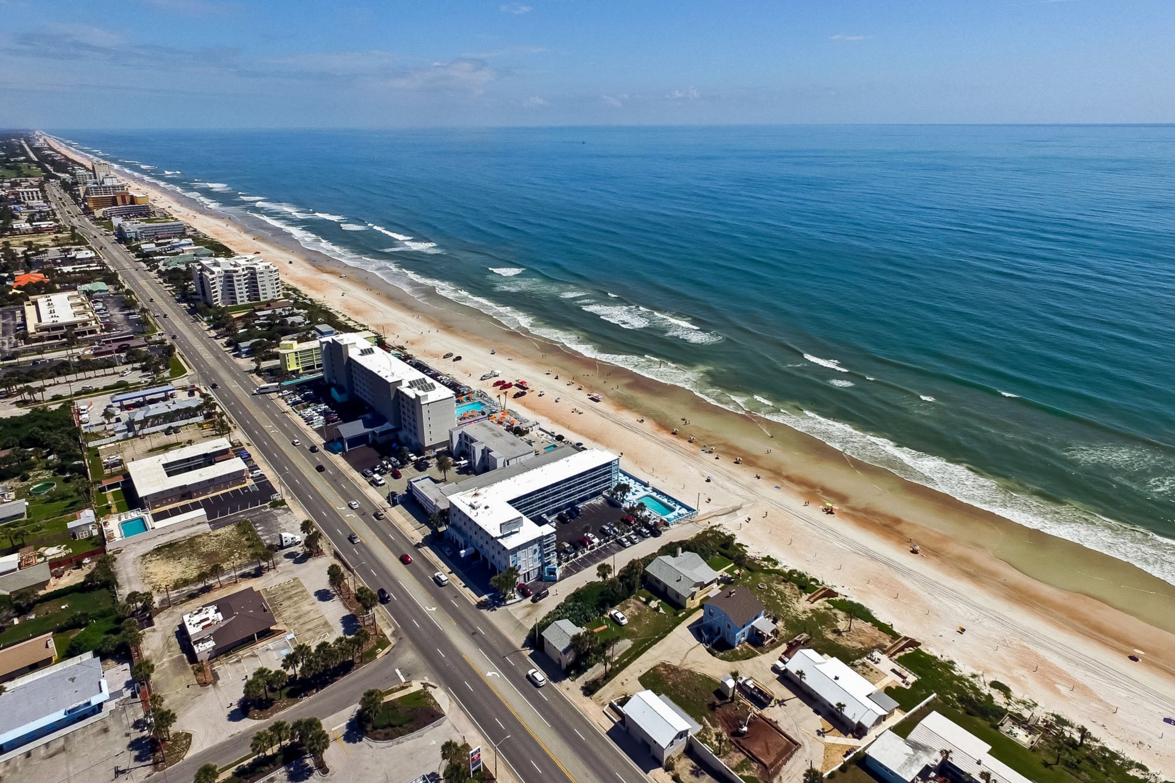 An aerial view of a coastal city with a beach, buildings, and a road.