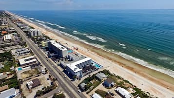 An aerial view of a coastal city with a beach, buildings, and a road.