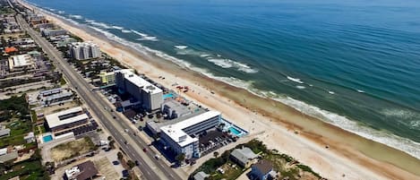 An aerial view of a coastal city with a beach, buildings, and a road.