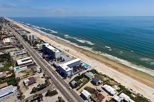 Vue aérienne d’une ville côtière avec une plage, des bâtiments et une route.