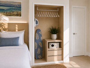 A bedroom with a bed, a closet with hanging clothes, an ironing board, a plant, and a door. - Chateau Mar Beach Resort (Ormond Beach)
