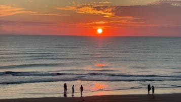 A sunset over the ocean with people on the beach.