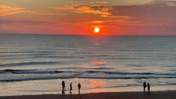 A sunset over the ocean with people on the beach.