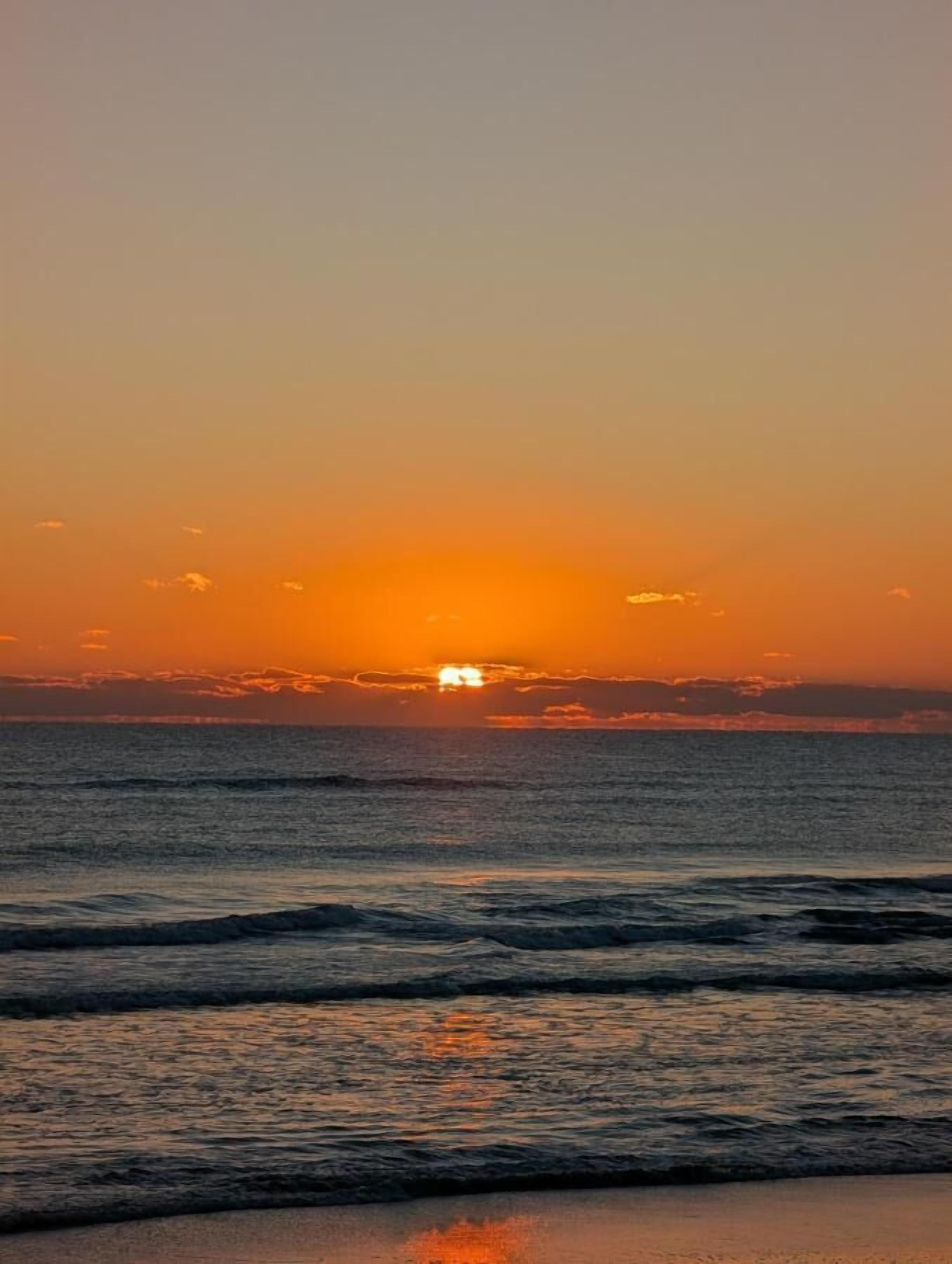 A sunset over the ocean with waves approaching the shore.