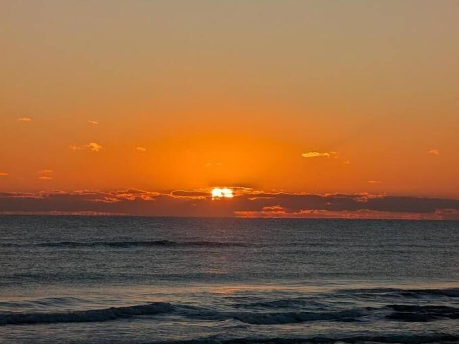 A sunset over the ocean with waves approaching the shore.