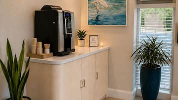 A reception area with a coffee machine, a painting of a bird, and potted plants.