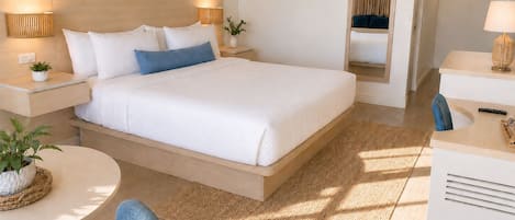 Ein Hotelzimmer mit einem großen Bett, Nachttischlampen, einem kleinen Tisch mit einer Pflanze, einem Sessel und einem Schreibtisch mit einer Lampe.