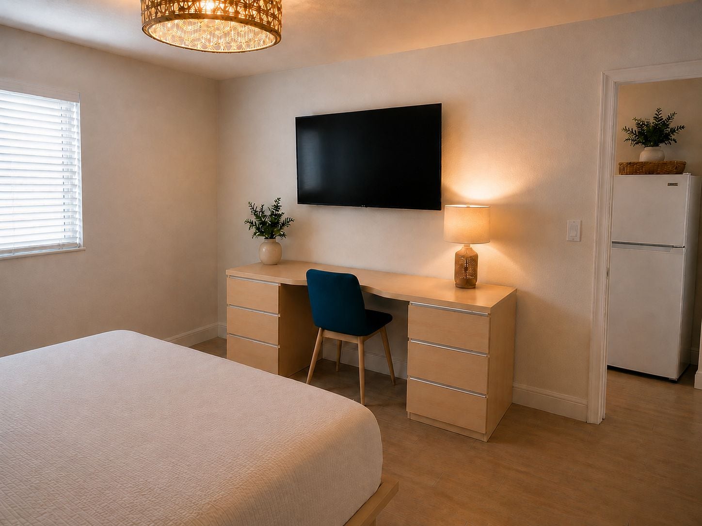 A bedroom with a bed, a desk with a chair, a television, a lamp, and a refrigerator.
