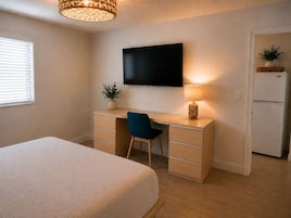 Une chambre à coucher comprenant un lit, un bureau avec une chaise, une télévision, une lampe et un réfrigérateur.