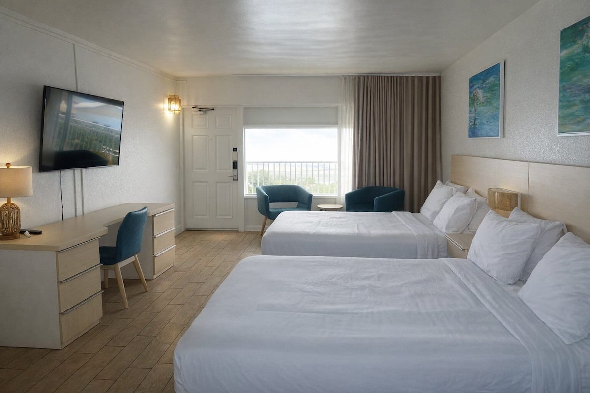 Une chambre d’hôtel avec deux lits, un bureau avec une chaise, une télévision et une fenêtre avec des rideaux.