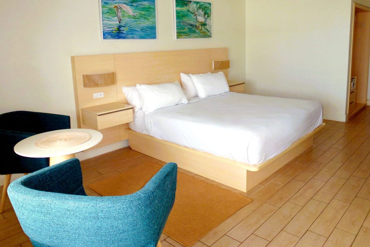 Une chambre d’hôtel avec un grand lit, une table de chevet, une chaise et deux tableaux au mur.