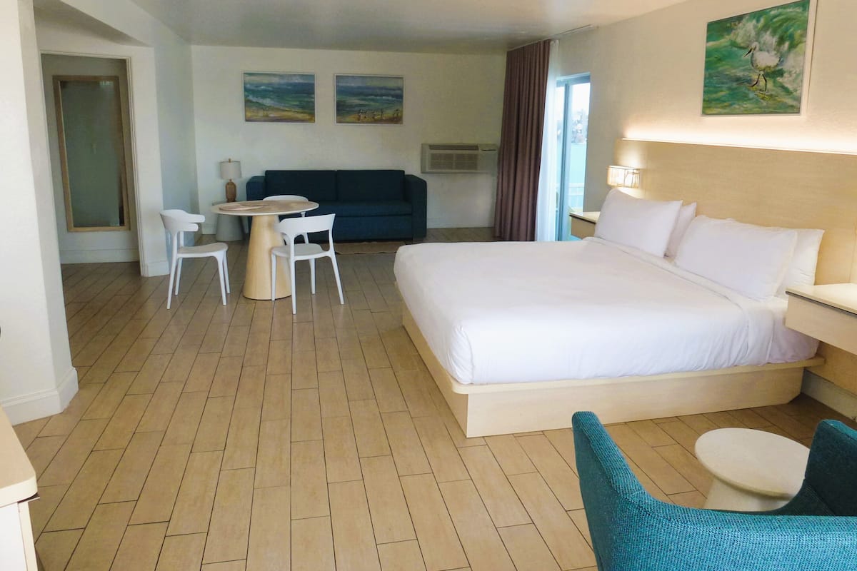 Une chambre d’hôtel avec un grand lit, une petite table avec des chaises, un canapé bleu et deux tableaux accrochés au mur.