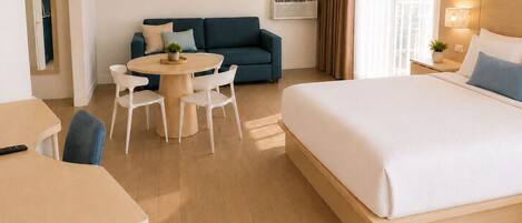 Una habitación de hotel con una cama, una mesa redonda con sillas, un sofá y dos cuadros colgados en la pared.