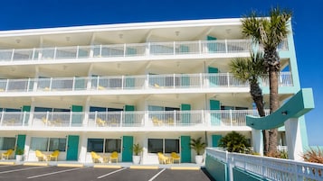 A multi-story hotel with balconies, yellow chairs, and a palm tree.