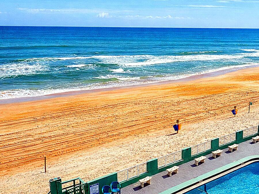 Una playa con zona de piscina, que incluye una piscina, sillas de descanso y una valla.