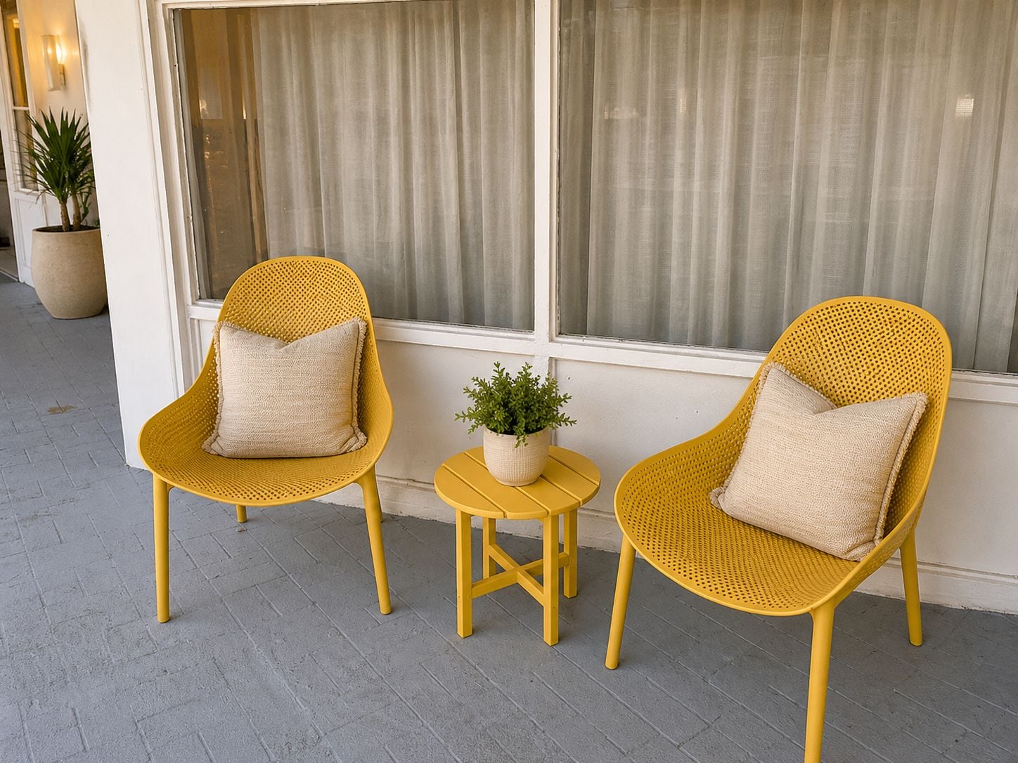 A seating area with two yellow wicker chairs and a small round table, accompanied by a potted plant.