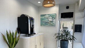 Een receptie met een koffieapparaat, een schilderij van een vogel en potplanten.