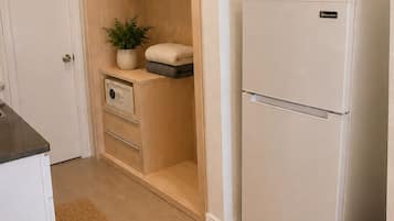 A kitchen with a white refrigerator, wooden cabinets, a built-in oven, a small plant, and a woven basket on top of the fridge.