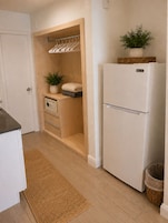 A kitchen with a white refrigerator, wooden cabinets, a built-in oven, a small plant, and a woven basket on top of the fridge.