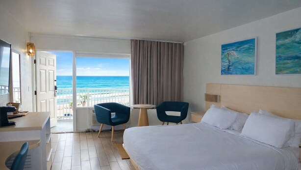 Een hotelkamer met een bed, twee stoelen, een bureau, een bijzettafeltje en uitzicht op de oceaan.