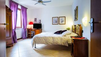 A bedroom with a bed, a desk, a chair, a television, and a ceiling fan.