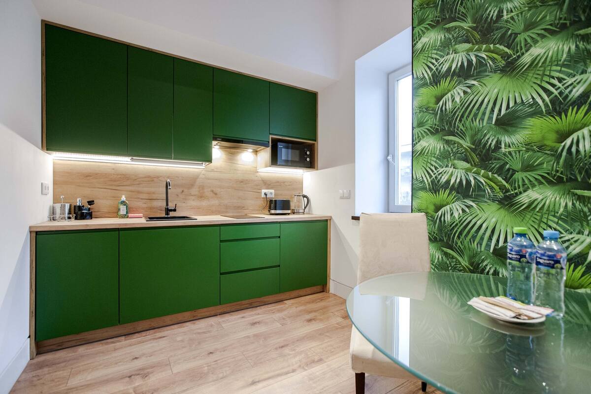 A modern kitchen with green cabinets, a microwave, and a glass table with a chair.
