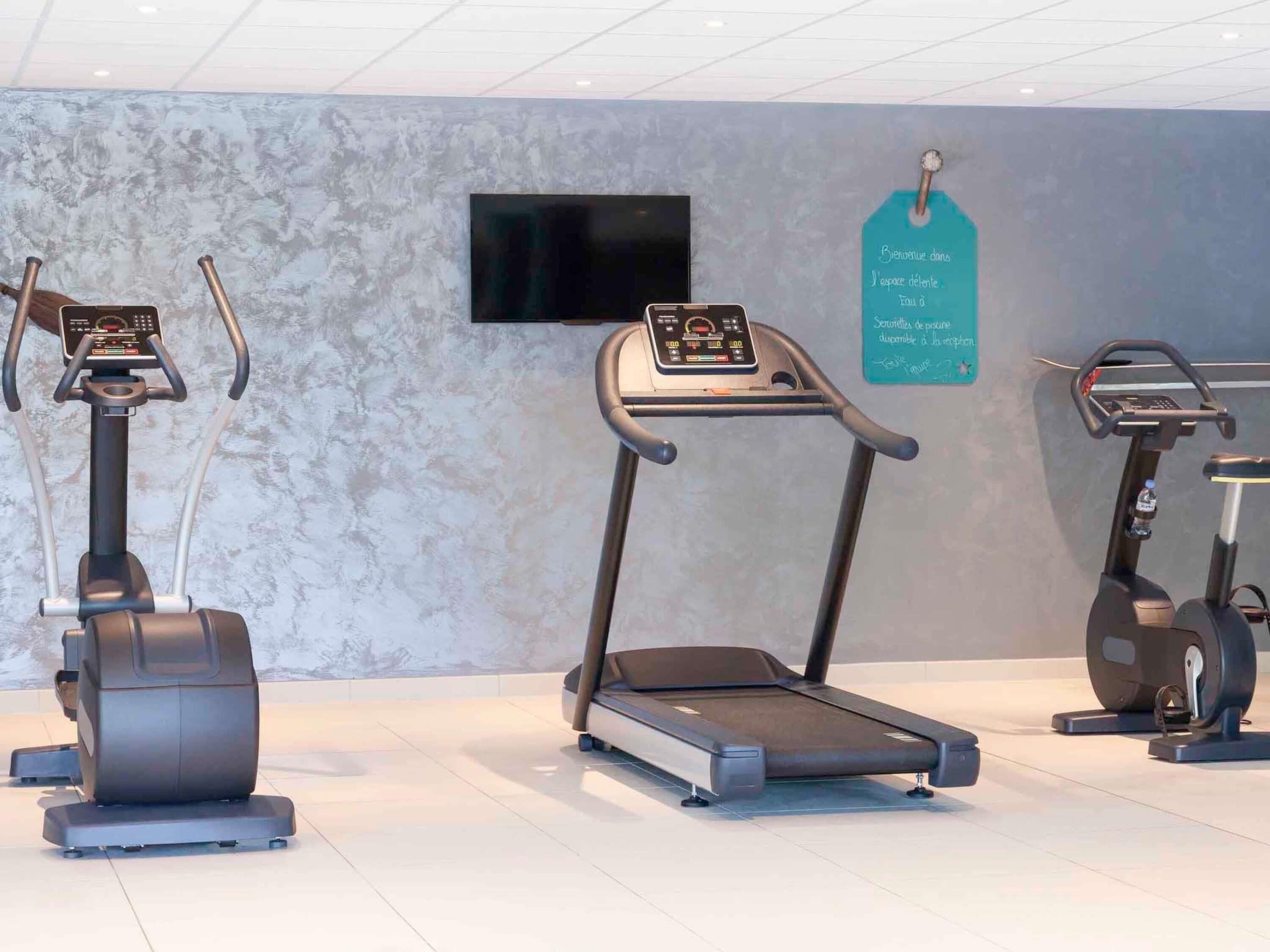 Un área de fitness con bicicletas estáticas, cinta de correr y televisor instalado en la pared.