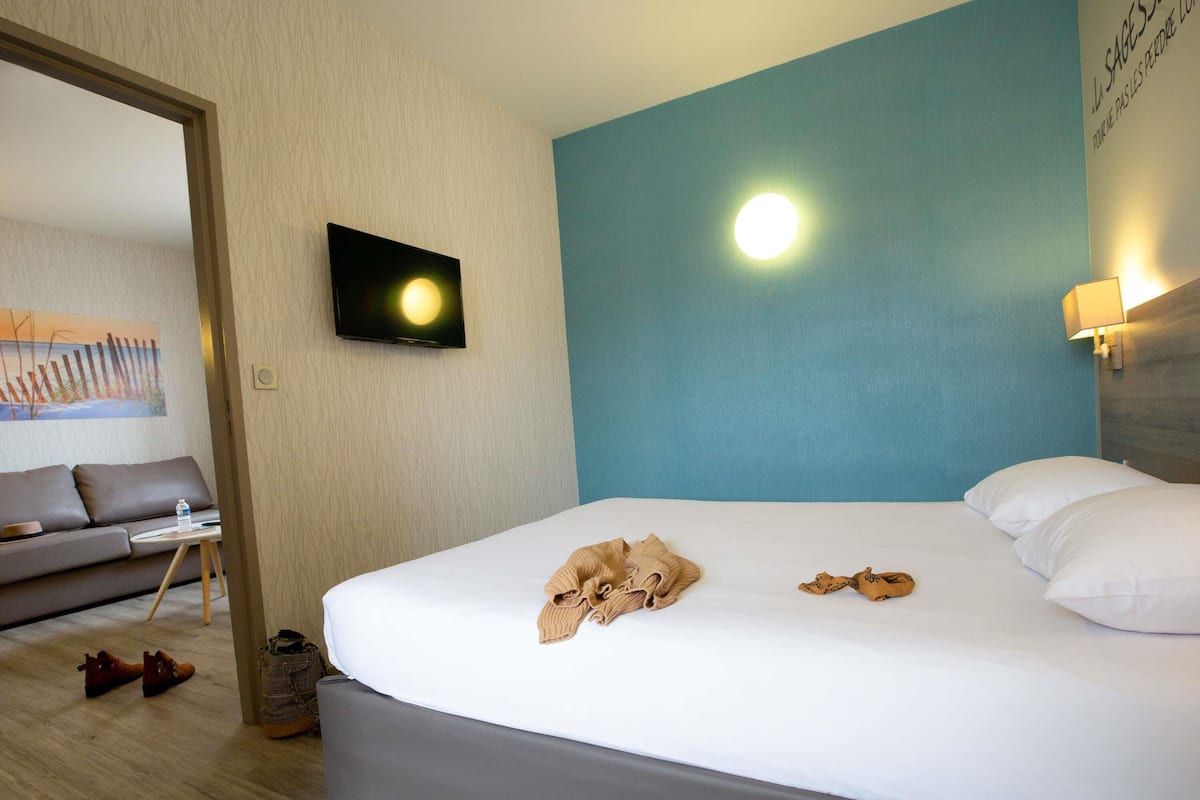 A hotel room with a bed, a television mounted on the wall, a sofa, and a small table.