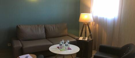 Et værelse med en brun sofa, to lænestole, et lille rundt bord med vandflasker, en lampe og en bærbar computer på et sofabord.