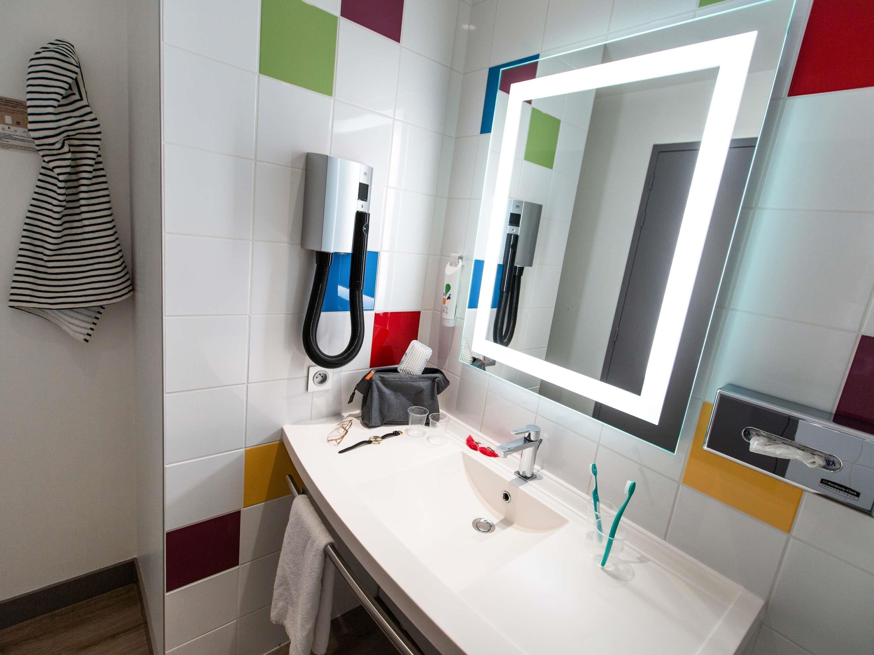 Een moderne badkamer met een witte wastafel, een grote spiegel, een handdouche en een handdoekrek.