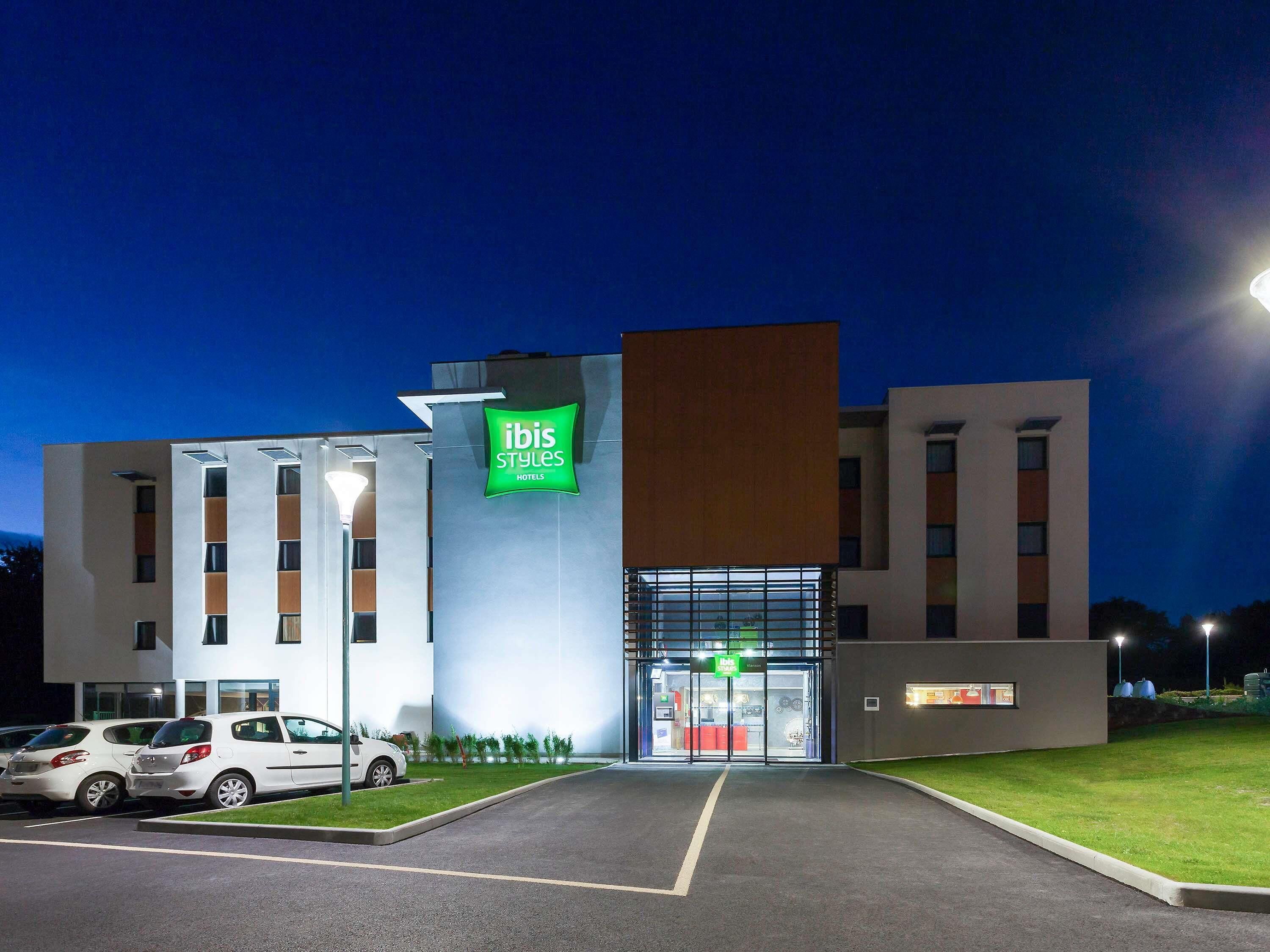 Un hotel moderno con un letrero verde llamativo, estacionamiento y una entrada bien iluminada.