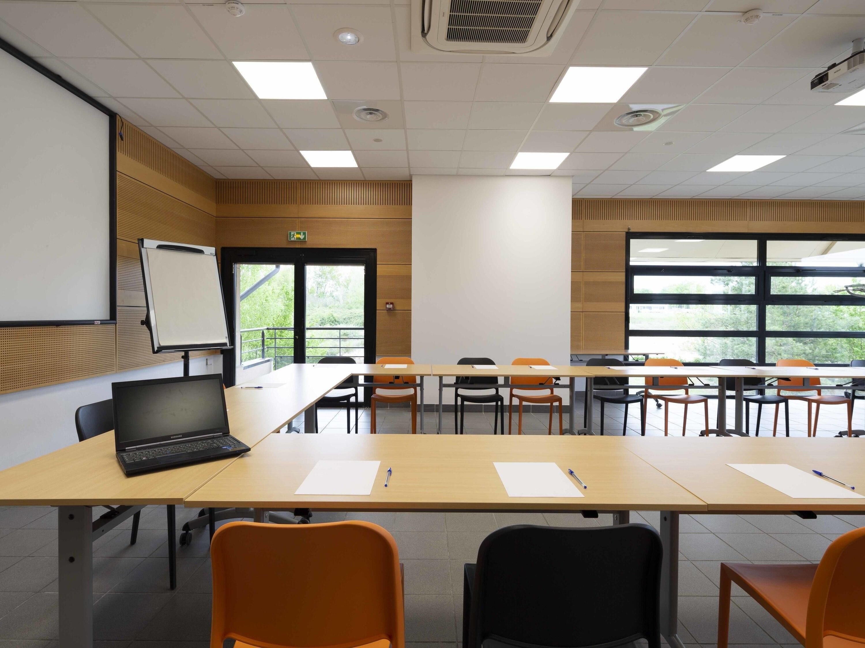 A conference room with a large table, chairs, a laptop, a whiteboard, and a projector screen.