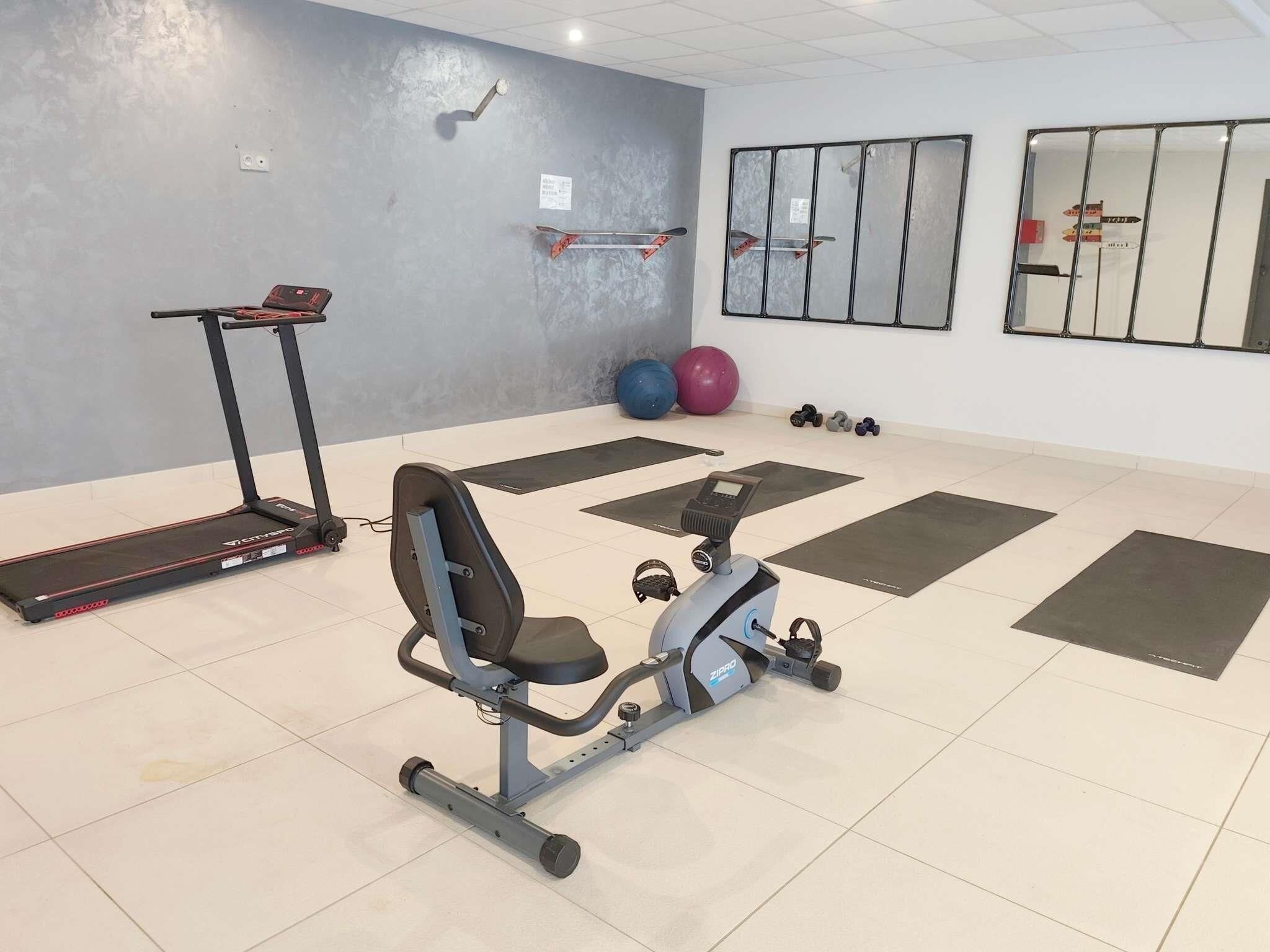 A gym with exercise equipment including a stationary bike, a treadmill, and free weights.