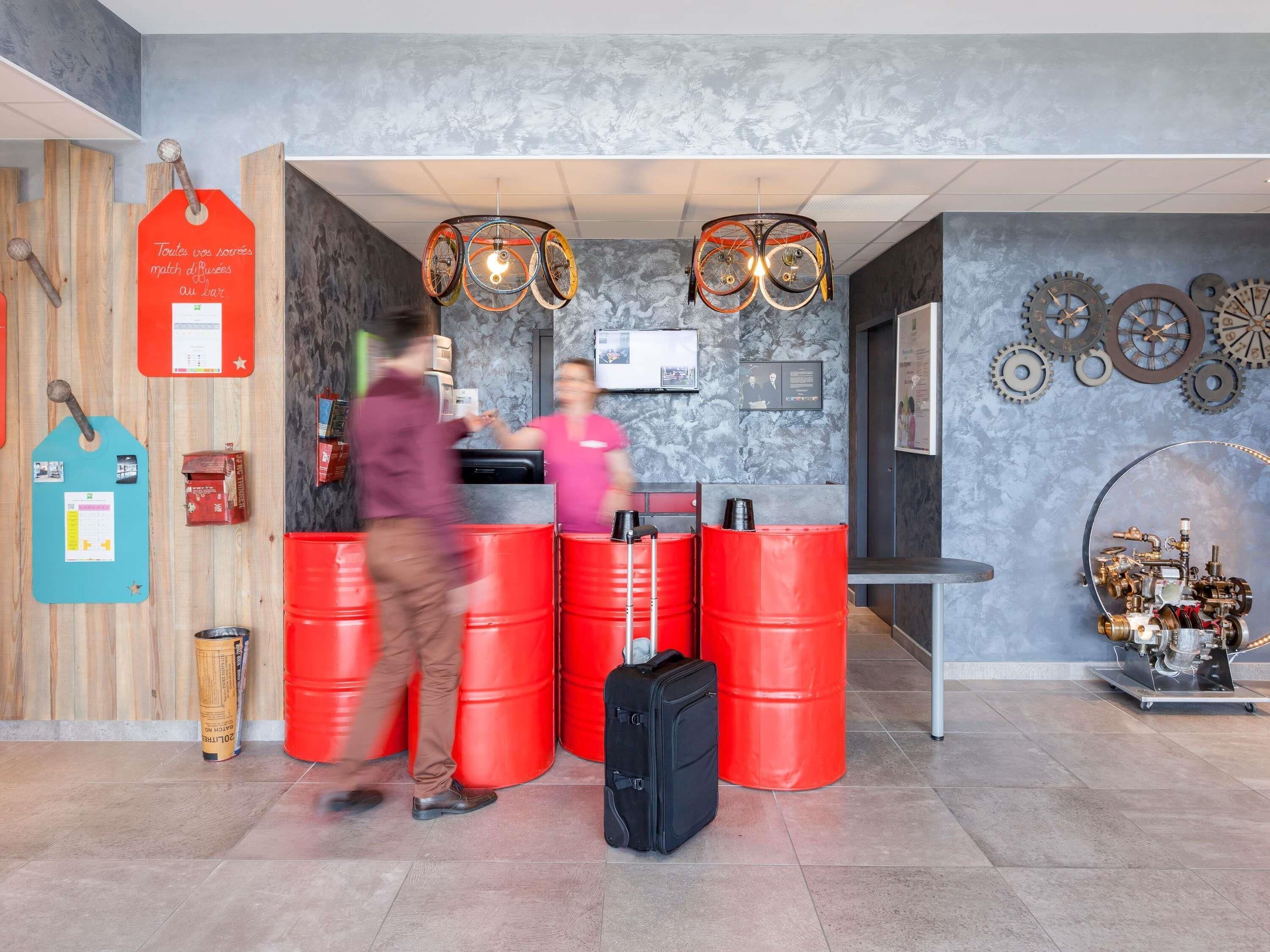 Un espace d’accueil avec un mur en bois, des barils rouges, une valise noire et un luminaire fixé au mur.