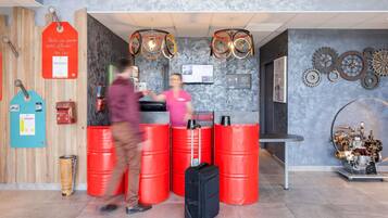 Un espace d’accueil avec un mur en bois, des barils rouges, une valise noire et un luminaire fixé au mur.